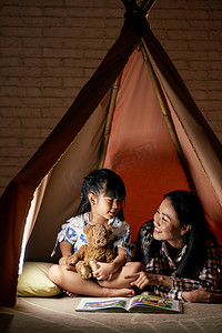 快乐的母亲和女儿在帐篷里玩耍, 看书