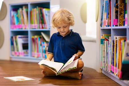 学龄前儿童摄影照片_学校图书馆里的孩子孩子们看书。小男孩读书和学习。书店的孩子们聪明的学龄前儿童选择借书.
