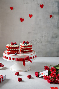 盘上有红绒心形蛋糕，背景上有红玫瑰。 情人节的概念。 甜蜜的礼物 面包店、糖果店