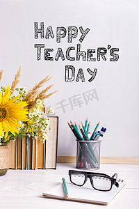 桌子上摆着花和笔记本，戴着眼镜。题词祝教师节快乐..