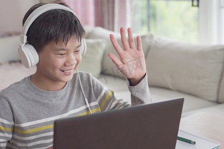 十几岁以下的男孩在家里用笔记本电脑进行面对面的视频通话，使用缩放在线会议应用程序，社交距离，在家学习，在covid-19 Coronavirus期间远程学习，新的正常概念