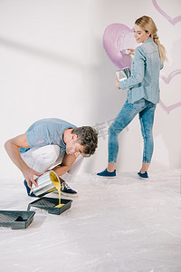 欧美建筑摄影照片_3.年轻男子在盘子里加入黄色颜料，而女友则在白墙上画粉红色的心