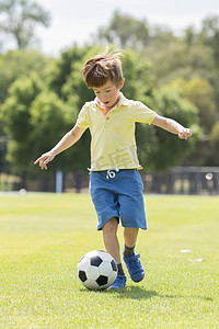 踢球的人摄影照片_小孩子7或8岁享受快乐踢足球足球在草市公园田野奔跑和踢球兴奋的童年运动激情