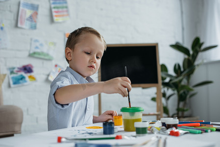 孩子气的摄影照片_聚焦的小男孩与刷子和绘画画图片独自在家