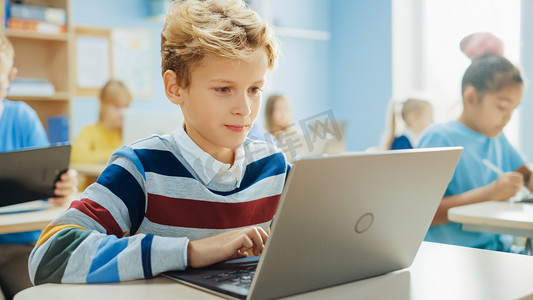 小学计算机科学课：聪明男孩使用笔记本电脑，他的同学也与笔记本电脑一起工作。在STEM 、游戏和学习中接受现代教育的儿童