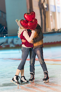 happy young couple with heart shaped balloons hugging on rink at st valentines day