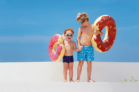 快乐的孩子在眼镜和游泳裤与甜甜圈橡胶戒指准备暑假