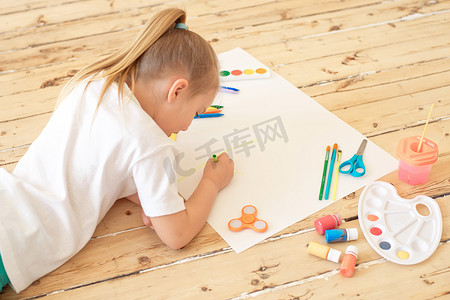 学前教育摄影照片_女孩躺在地板上绘画用品和绘画在白纸上