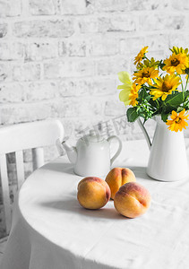 成熟的桃子和一束黄色的花在桌子上的光背景。舒适的家庭厨房静生活