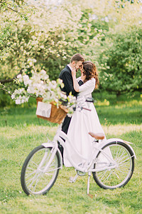 开心摄影照片_性感的年轻新婚夫妇在公园里互相抱住。前景上配有婚礼装饰的自行车