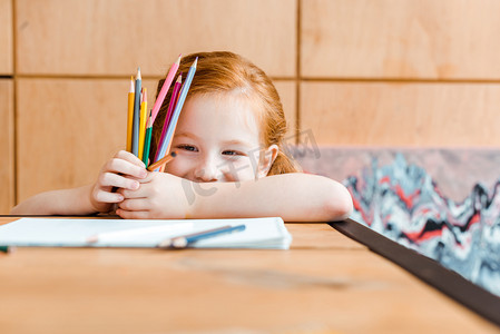 创意坚持摄影照片_带着彩色铅笔的红头发孩子的选择性聚焦 