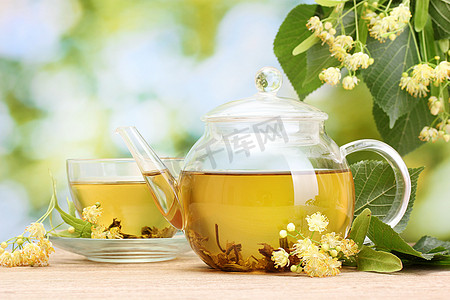 茶壶和林登茶和花朵在庭院里的木桌上的杯子