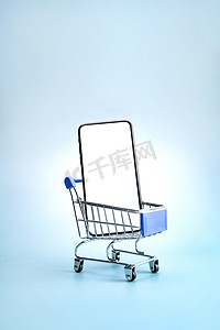 大促蓝色背景摄影照片_购物车和空白屏幕的手机