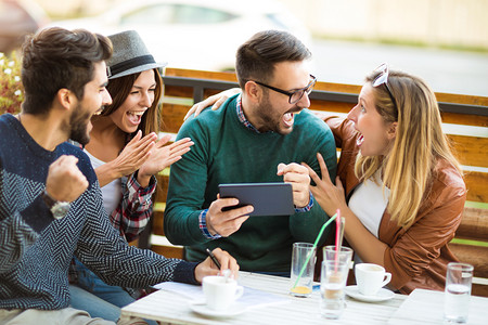 四组朋友一起喝咖啡。两个女人和两个男人在咖啡馆说笑, 享受他们的时间使用数字平板电脑.