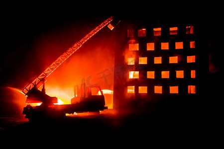 在夜里扑灭一栋私人房子的大火。玩具消防车与长的梯子和燃烧的建筑物在夜间。火警警报概念。选择性聚焦