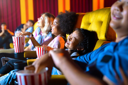 这个女孩和一群孩子坐在电影院的座位上看电影。脸上洋溢着快乐和欢乐.