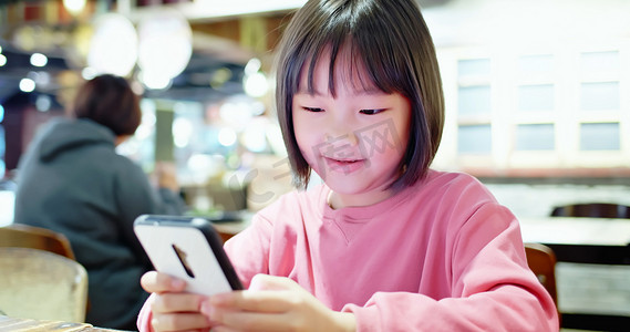 亚洲女孩在餐馆玩手机游戏，开心地笑着