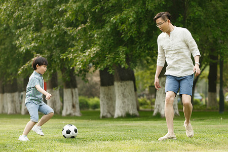 足球动作摄影照片_快乐父子在草地上踢足球