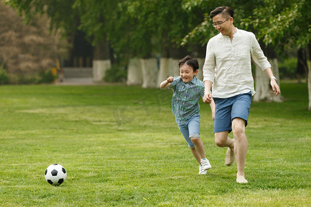 儿童踢足球摄影照片_快乐父子在草地上踢足球