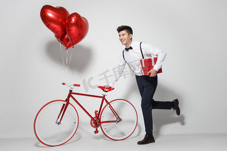 彩色爱心背景摄影照片_青年男人推着自行车跑