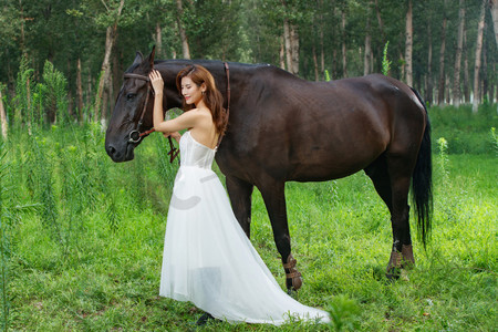 眼睛度假摄影照片_树林里漂亮的青年女人和马