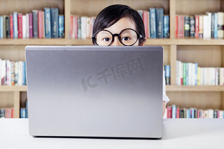 Child with laptop on desk peeping in library