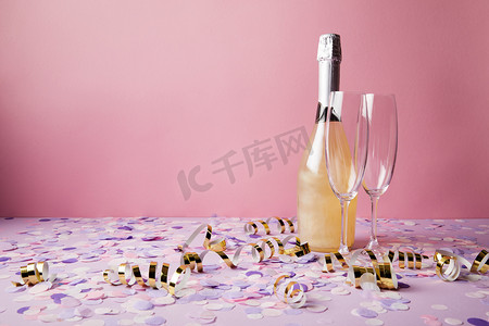 confetti摄影照片_bottle of champagne, glasses and confetti pieces on violet tabletop