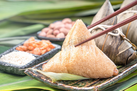 close摄影照片_Close up, copy space, famous chinese tasty food in dragon boat (duan wu) festival, steamed rice dumplings pyramidal shaped wrapped by bamboo leaves made by sticky rice raw ingredients