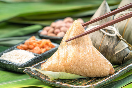 Close up, copy space, famous chinese tasty food in dragon boat (duan wu) festival, steamed rice dumplings pyramidal shaped wrapped by bamboo leaves made by sticky rice raw ingredients