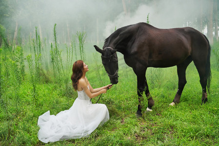 眼睛度假摄影照片_草地上穿婚纱的青年女人牵着马
