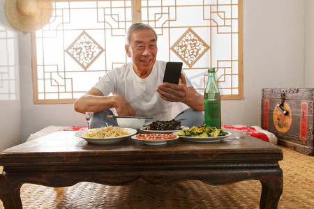 吃饭乡村摄影照片_老年人坐在家里吃饭看手机
