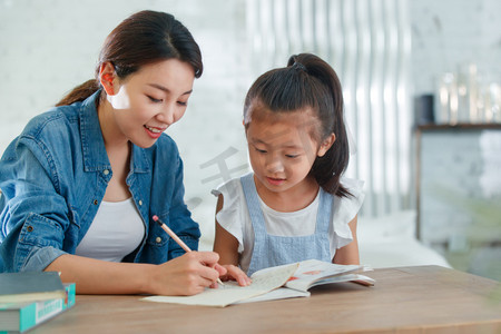 公寓住宅摄影照片_辅导女儿做作业的青年女人