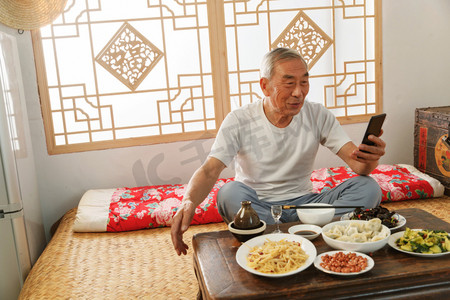 老年人坐在家里吃饭看手机