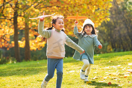 学龄儿童摄影照片_拿着玩具飞机在公园玩耍的女孩