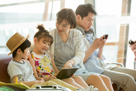 的行李箱摄影照片_快乐家庭在机场候机厅里使用电子产品