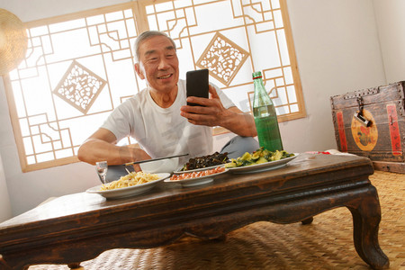 老年人坐在家里吃饭看手机
