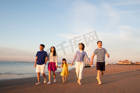 散步摄影照片_夕阳下在海边散步的幸福家庭