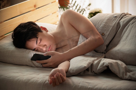 情侣室内摄影照片_躺在床上玩手机的年轻男人