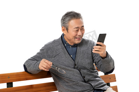 背景人物摄影照片_坐在长椅上的老人看手机