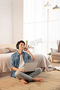 情侣衬衫摄影照片_年轻的男青年坐在地板上使用笔记本电脑