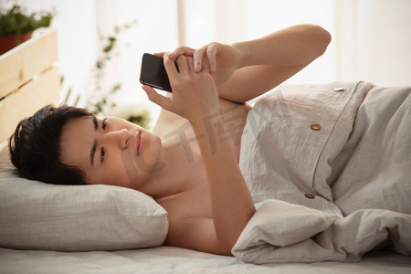 躺着的人像摄影照片_躺在床上玩手机的年轻男人