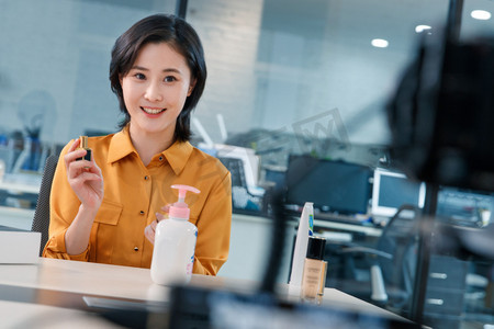 电商直播间背景摄影照片_青年女人在线直播销售化妆品