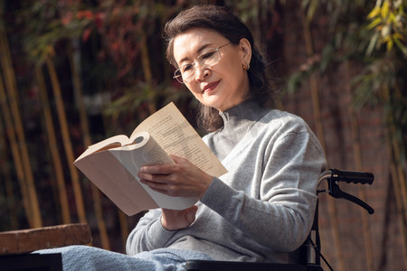 户外老年女人坐在轮椅上看书