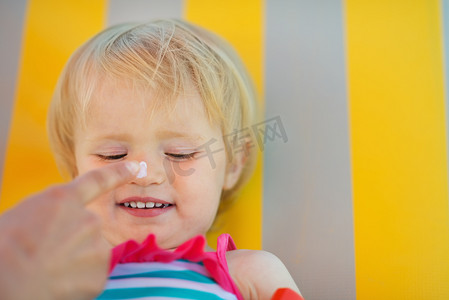 母亲的手在宝宝的鼻子上应用防晒霜