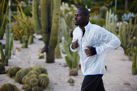 sport摄影照片_Young fit man in white windbreaker running fast in beautiful park, autumn sport outdoors, attractive dark skinned jogger training outdoors at beautiful evening, sport and healthy living concept