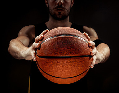 手臂侧面摄影照片_一名拿着篮子球在黑色背景上的篮球运动员的剪影视图