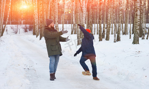 两个年轻人在冬天公园散步。其中一人滑倒, 失去平衡, 挥舞双臂, 后退, 他的朋友想支持它.