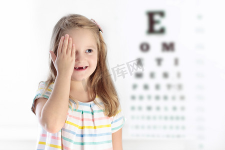 镜片摄影照片_孩子眼睛视力测试。孩子在 optitian。孩子们的的眼镜.