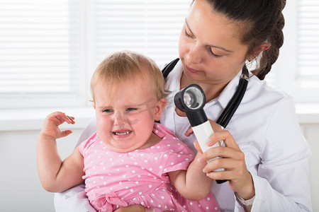 关闭一个女医生检查的耳朵哭泣的小女孩与皮镜