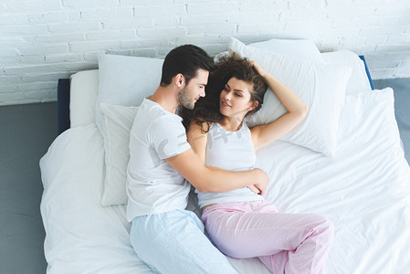 在床上躺在睡衣上的快乐的年轻夫妇的顶级视图 